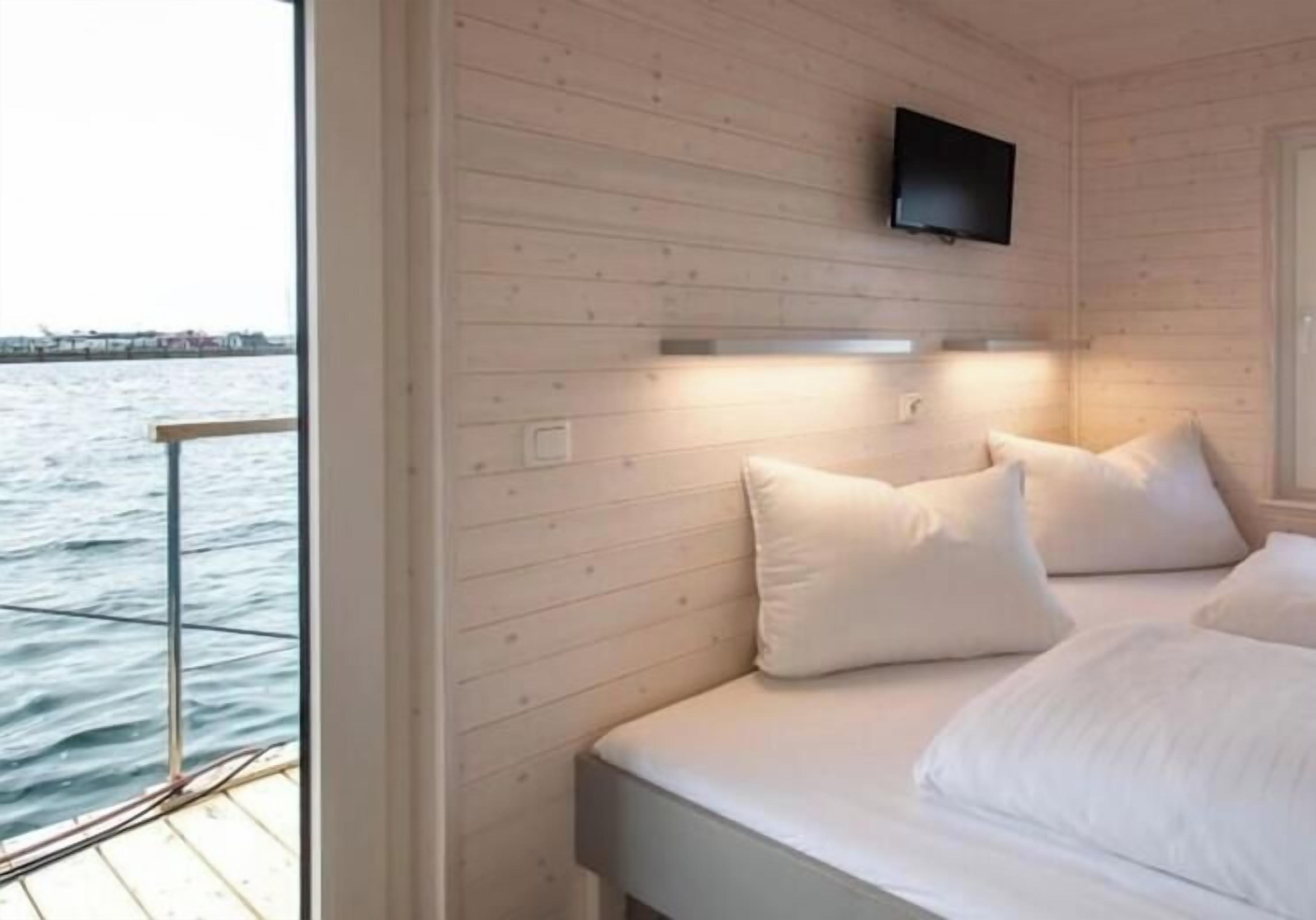 A cabin with a bed, a mounted television, and a view of the water.