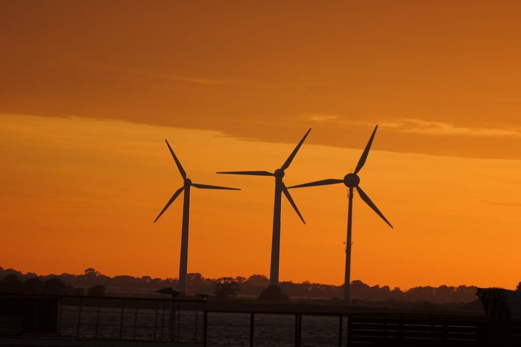 Drei Windkraftanlagen vor einem Sonnenuntergangshimmel.