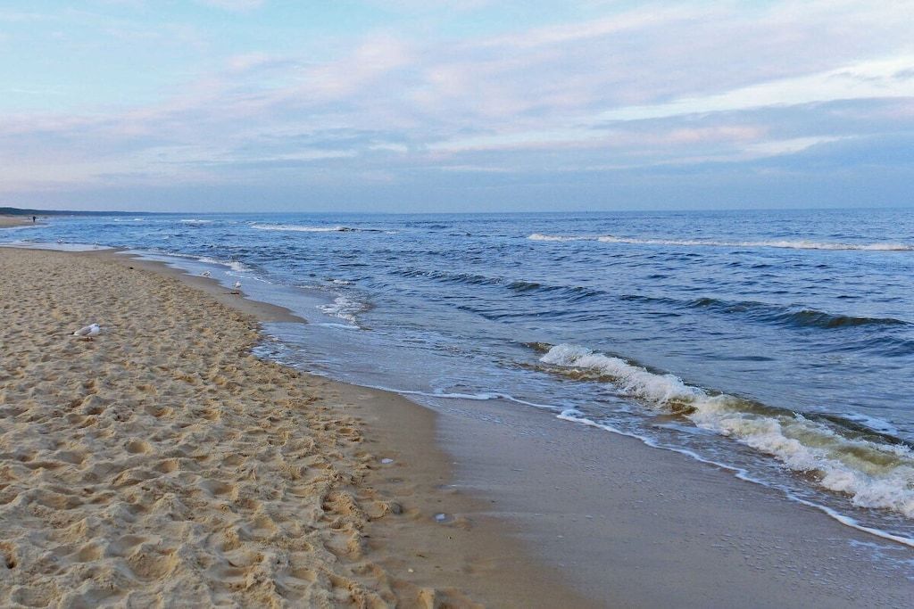 Ein sandiger Strand mit sanften Wellen, einem klaren Himmel und einer entfernten Küstenlinie.