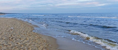 Ein sandiger Strand mit sanften Wellen, einem klaren Himmel und einer entfernten Küstenlinie.