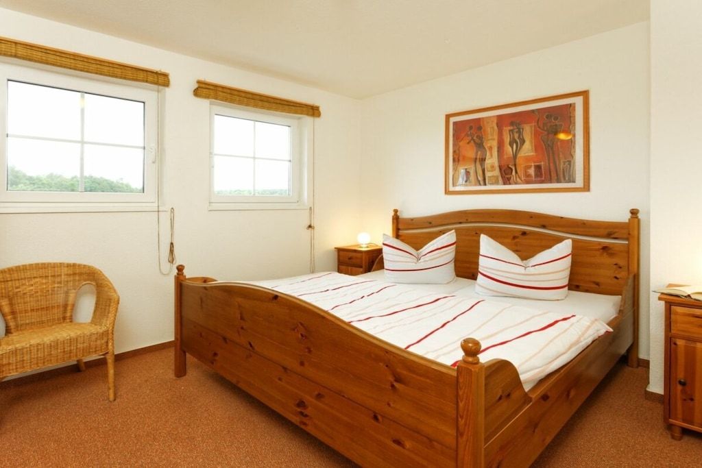 Un letto singolo con struttura in legno, due comodini, una sedia in vimini e un quadro appeso al muro.