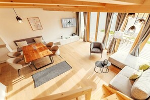 A modern living room with a wooden coffee table, sofa, and chairs. There is a television mounted on the wall and a window with curtains. - Cabin in Niederwölz with sauna (Niederwölz)