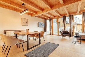 A modern interior with a wooden ceiling, a dining area with a table and chairs, a sofa, and a large window with curtains. - Cabin in Niederwölz with sauna (Niederwölz)