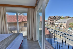 A balcony with a bed, curtains, and a view of buildings and a street. - Micheline Hotel Tricot (Gramado)