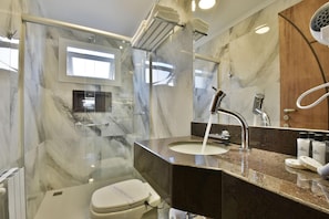 A modern bathroom with a glass-enclosed shower, a marble-tiled wall, a sink with a faucet, and a toilet. - Micheline Hotel Tricot (Gramado)