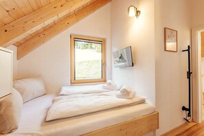 A bedroom with two beds, a wooden ceiling, a window, and a wall-mounted TV. - Cabin in Niederwölz with sauna (Niederwölz)