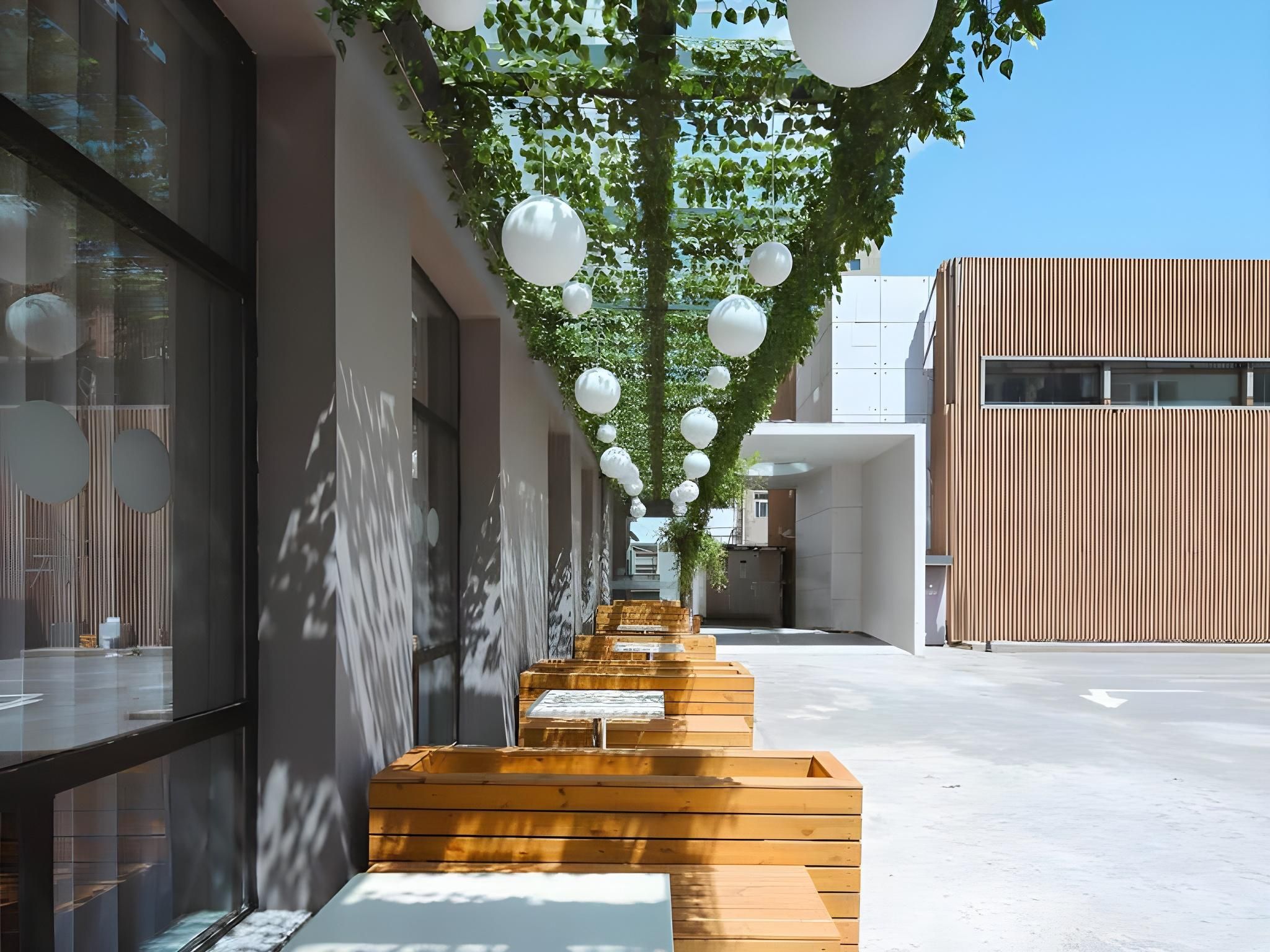 A modern building with a wooden bench area, white spherical decorations, and a clear sky.