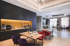 Un espace repas moderne, doté de tables et de chaises, d’un coin café et offrant une vue sur la pièce adjacente.
