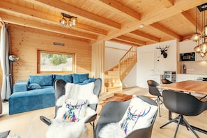 A modern interior with a wooden ceiling, a blue sofa, a dining area with chairs, and a staircase. - Chalet #1 with 2 bedrooms and sauna (Niederwölz)