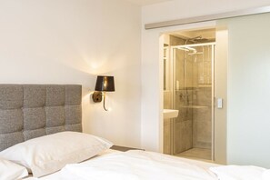 Une chambre à coucher avec une tête de lit capitonnée, une lampe de chevet et une douche fermée par des parois de verre.