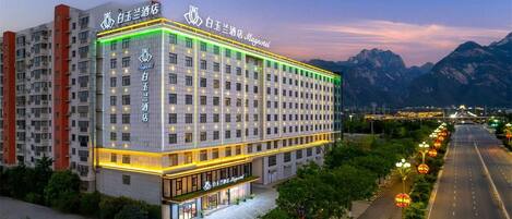 A multi-story hotel with a prominent entrance and a view of mountains in the background.