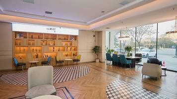 A modern hotel lobby with a wooden reception desk, seating area, and large windows offering a view of the street.