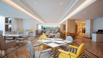 A modern dining area with multiple tables and chairs, a kitchen area, and a view of the sea.