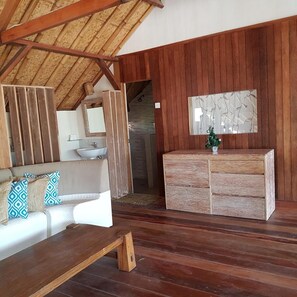 Una habitación con techo de madera, un sofá con cojines estampados, un banco de madera, un armario de madera y un espejo montado en la pared.
