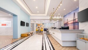 A modern hotel lobby with a reception desk, seating area, and a large wall mural. - Magnotel (Qionghai)