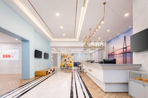 Eine moderne Hotelhalle mit einer Rezeption, einer Sitzgelegenheit und einem großen Wandbild.