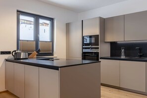 A modern kitchen with a central island, built-in appliances, and a window with blinds. - Apartment with 1 bedroom (St. Martin am Tennengebirge)