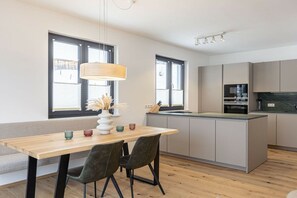 A modern kitchen with a central island, built-in appliances, and a dining area with a wooden table and chairs. - Apartment with 1 bedroom (St. Martin am Tennengebirge)