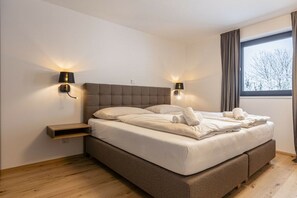 Une chambre à coucher moderne avec un grand lit, deux lampes de chevet, une fenêtre avec des rideaux et un plancher en bois.