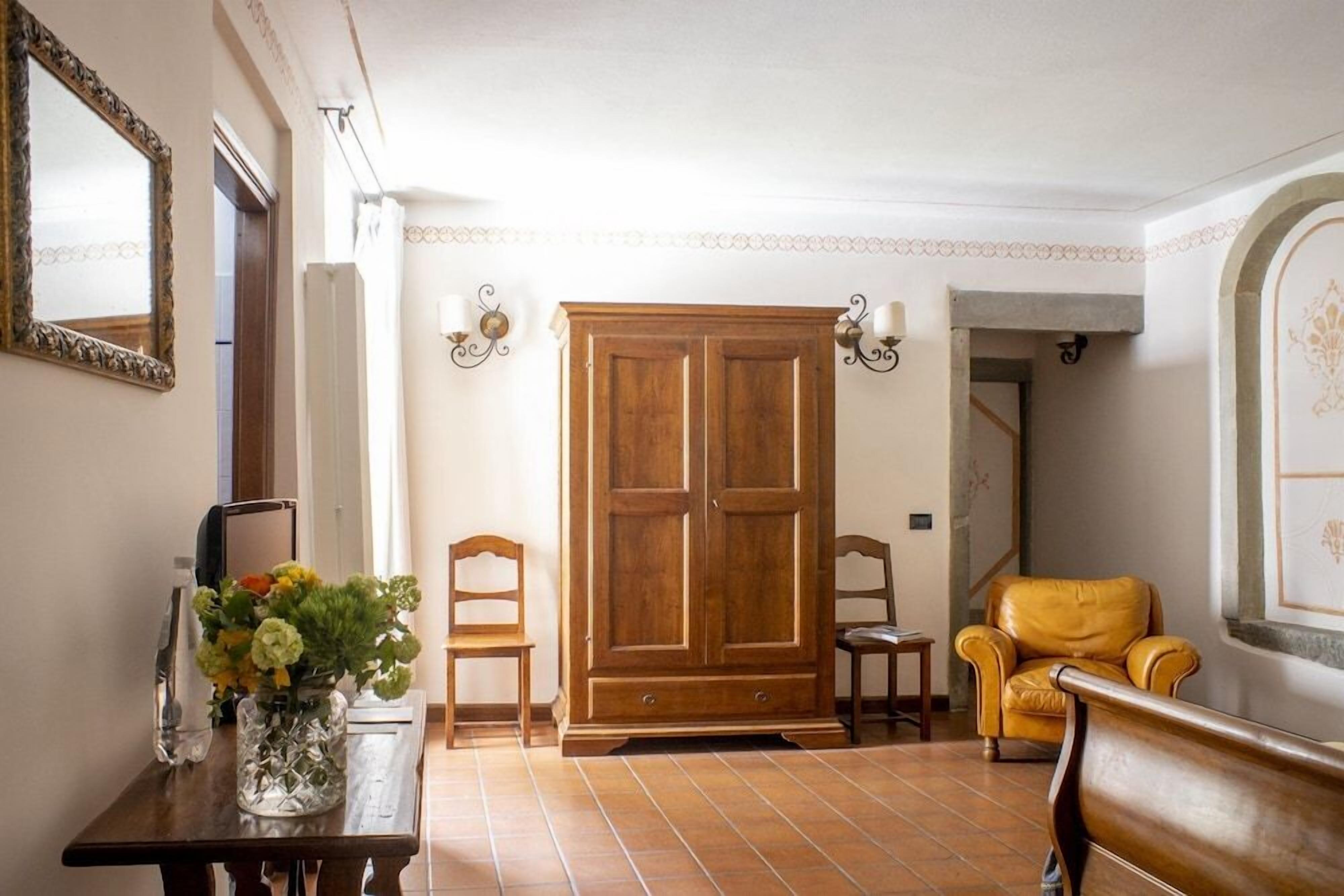 A room with a wooden wardrobe, a table with a vase of flowers, two chairs, and a bench.