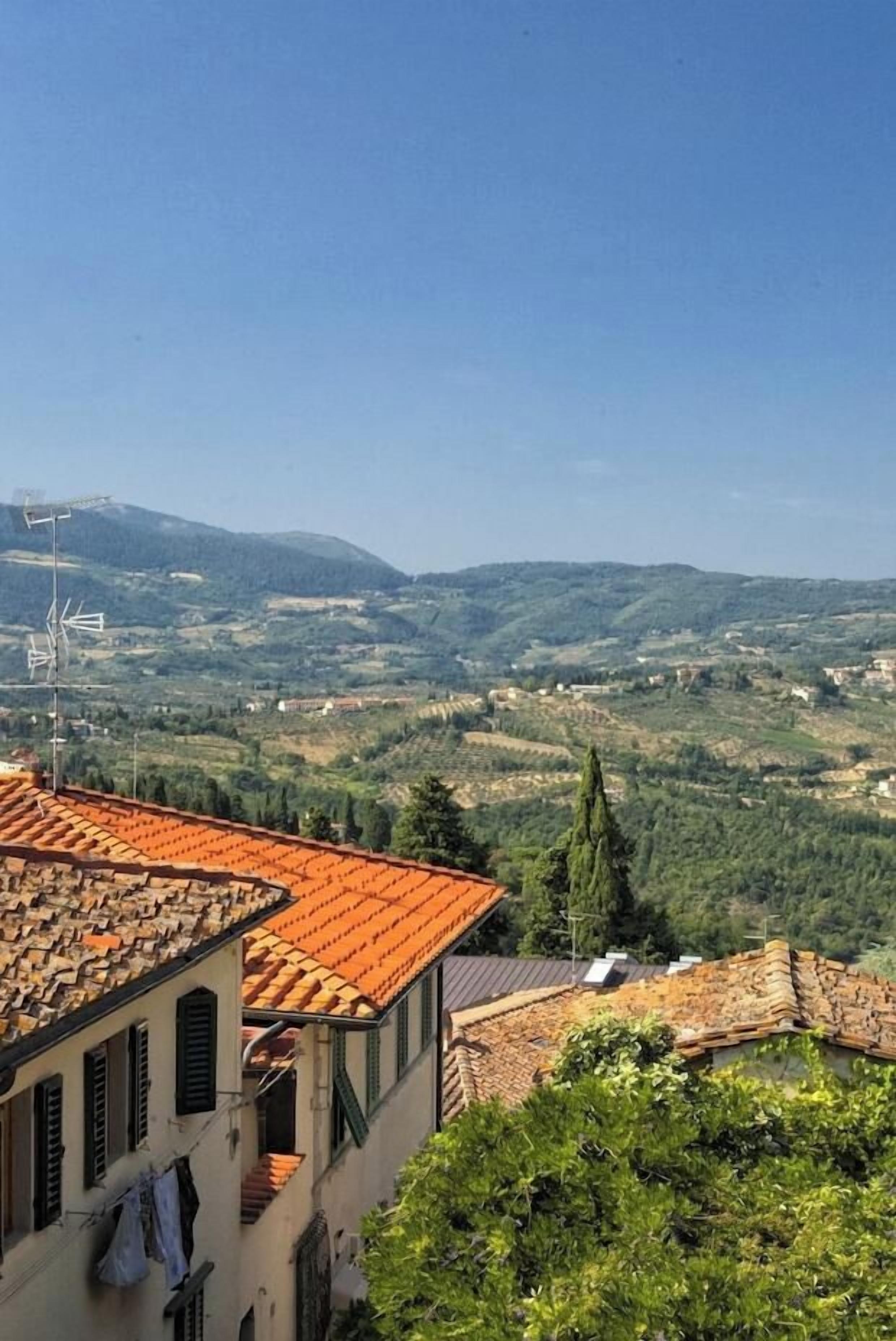 A building with a red-tiled roof, a balcony, and a view of a hilly landscape.