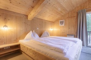 Quarto de cabana de madeira com cama, mesa pequena e janela com cortinas.