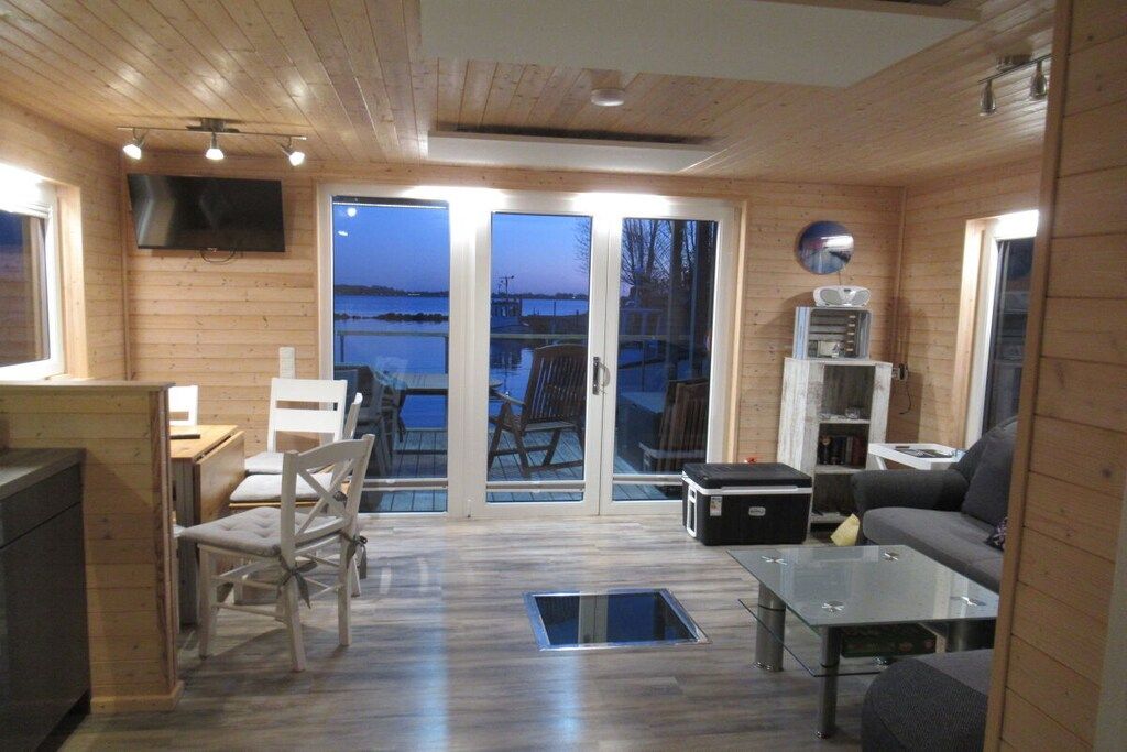 A wooden interior with a sofa, chairs, a table, a TV, and a view through glass doors to the outside.