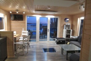 A wooden interior with a sofa, chairs, a table, a TV, and a view through glass doors to the outside. - Houseboat Kaddi's Sunflower - House & Sea (Fehmarn OT Burgstaaken)