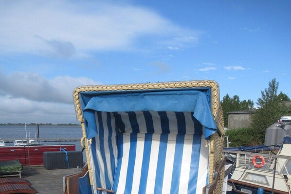 A covered seating area with a striped awning, a wooden deck, and boats in the background.