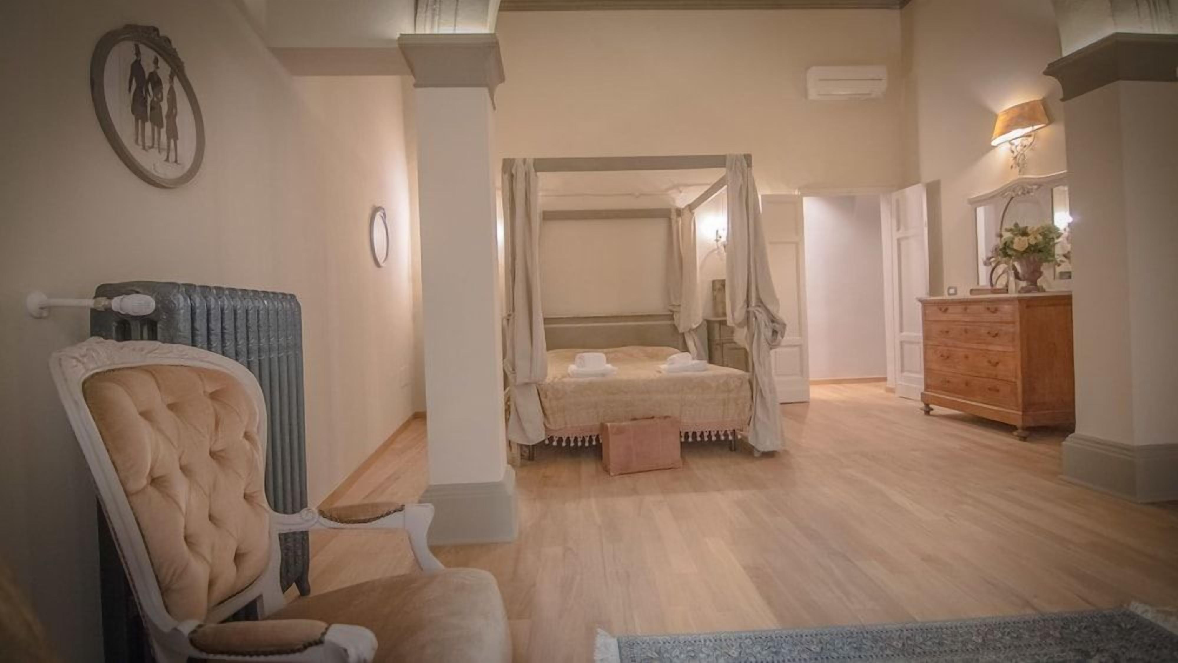 A bedroom with a four-poster bed, a wooden dresser, and a chair.