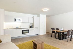 A modern kitchen with white cabinets, a microwave, and a dining area with a wooden table and chairs. - Apartment in Radstadt with swimming pool (Radstadt)