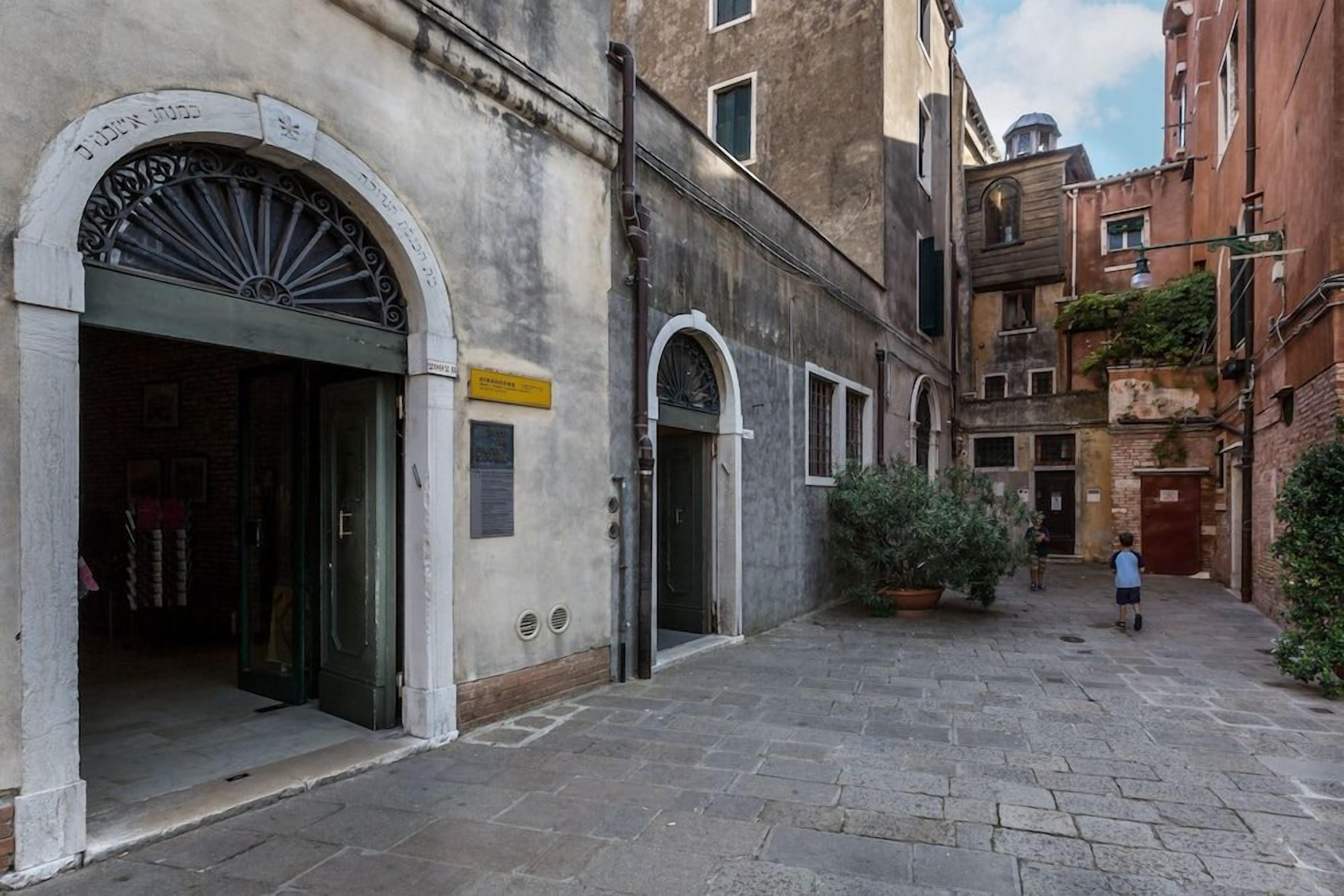 A narrow street with buildings on either side, a clear sky, and a child walking.