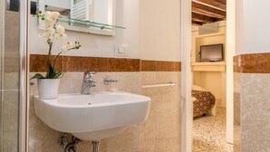 A bathroom with a white sink, a glass shelf, a potted plant, and a shower area. - San Marco Joy (Venice)