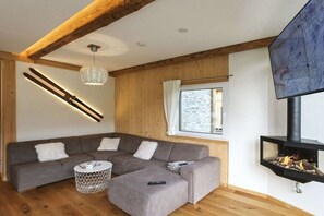 En moderne stue med en hjørnesofa, et rundt sofabord, en pejs og et fjernsyn monteret på væggen.