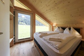 A bedroom with a bed, pillows, and a view of a grassy field through a large window. - Cabin in Murau with sauna and terrace (Murau)
