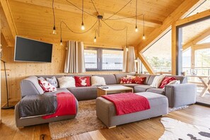 A modern log cabin interior with a sectional sofa, a flat-screen TV, and a large window. - Cabin in Pichl near Schladming with sauna (Pichl bei Schladming)