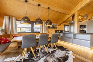 A modern interior with a wooden ceiling, a dining area with a table and chairs, and a kitchen with built-in appliances. - Cabin in Pichl near Schladming with sauna (Pichl bei Schladming)