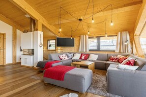 Ein gemütliches Wohnzimmer mit Holzbalkendecke, einer Sofagarnitur, einem Fernseher und einem Kamin.