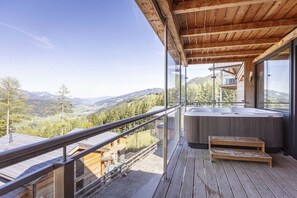 A wooden deck with a hot tub, glass railings, and a view of mountains. - Cabin in Pichl near Schladming with sauna (Pichl bei Schladming)