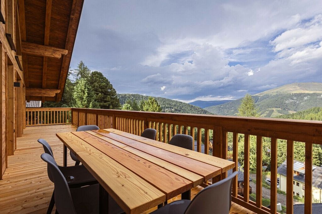 Eine Holzterrasse mit Tisch und Stühlen, mit Blick auf eine gebirgige Landschaft.