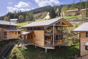 Eine moderne Holzcabin mit Glasbalkon, umgeben von bewaldeter Landschaft.