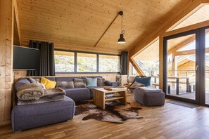 Ein modernes Interieur einer Blockhütte mit einer Couch, einem Hocker, einem Couchtisch und einem großen Fenster.