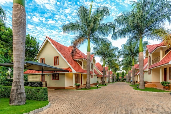 Una hilera de casas con techos rojos y palmeras, un sendero pavimentado y un cielo despejado.
