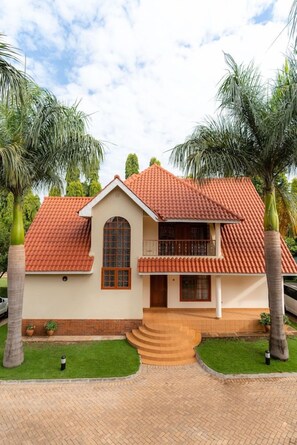 A two-story house with a red-tiled roof, a central arched window, and a small balcony. - Kibo Homes Moshi (Moshi)