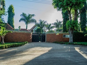 Un camino de entrada con puerta pasa a un edificio con un muro de ladrillo y una palmera.
