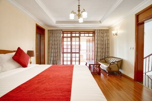 A hotel room with a large bed, a red throw, a chandelier, a wooden chair, and a view through a glass door. - Kibo Homes Moshi (Moshi)