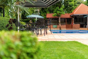 Un patio exterior con piscina, rodeado de follaje y un edificio con tejado de tejas rojas.