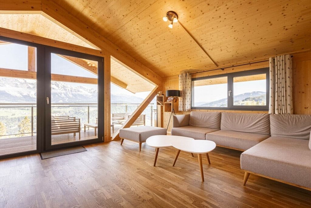 Un intérieur en bois avec un canapé, une table basse et une vue sur les montagnes, visible à travers de grandes fenêtres.