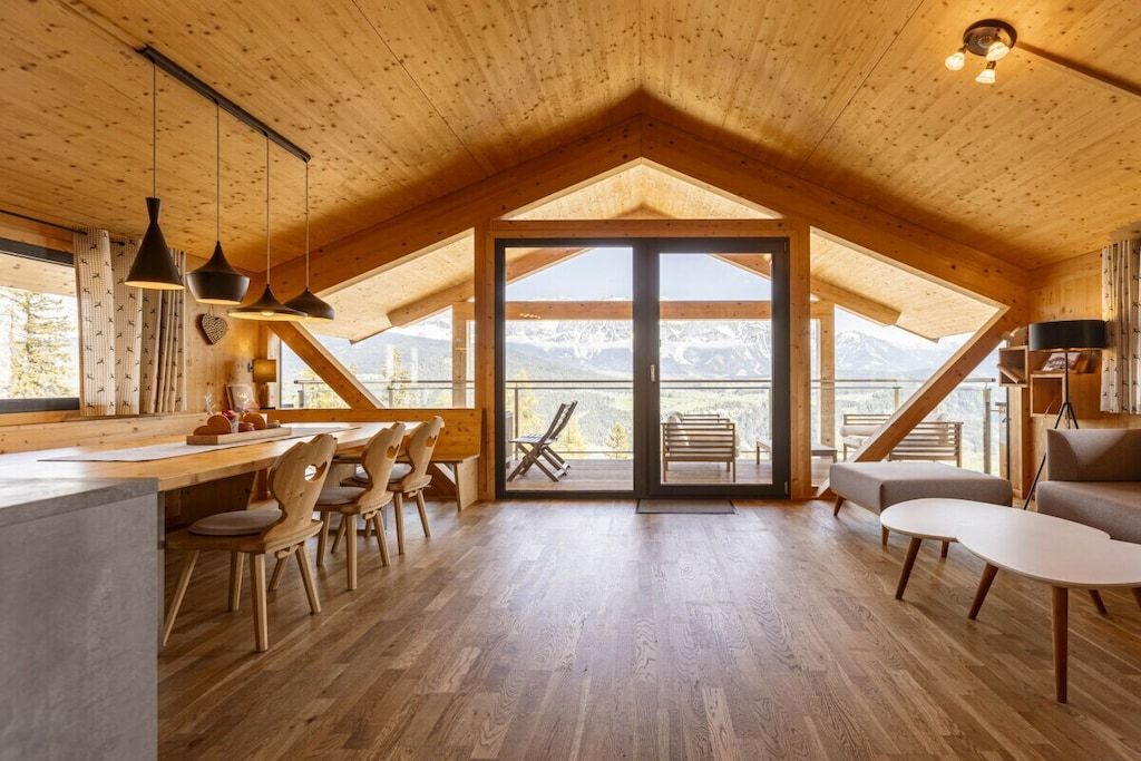 A spacious loft-style room with a wooden ceiling, a dining area with chairs and a table, and a seating area with sofas and a coffee table.