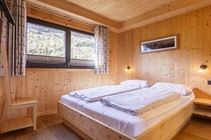 Una habitación de cabaña de madera con dos camas, una ventana con cortinas, un cuadro en la pared y un pequeño banco.